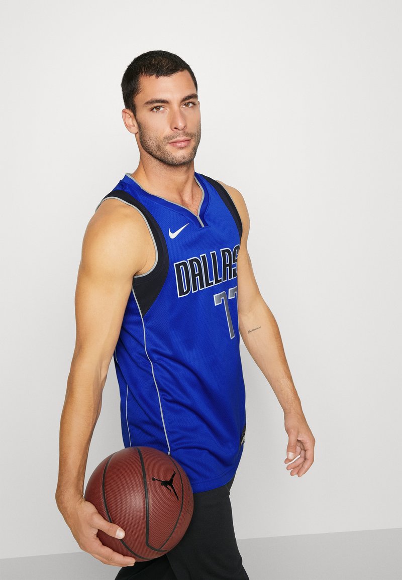 Niebieski strój koszykarski z czarnymi akcentami, z napisem "DALLAS" w białym kolorze, w zestawie z brązową piłką koszykarską z czarnym logo.