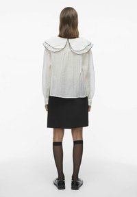 Blusa blanca de manga larga con un gran cuello en capas y borde negro, combinada con una falda negra y calcetas de red hasta la rodilla.