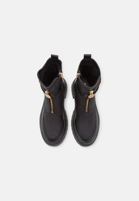 Botas negras hasta el tobillo con cremalleras doradas, con un empeine de cuero suave, suela de goma y cuello acolchado, que exhiben un diseño de punta redonda.