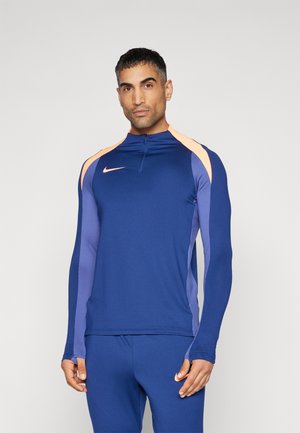 Top sportivo blu navy con zip a metà e maniche lunghe, con accenti arancioni e viola sulle spalle e sui pannelli laterali. Logo Nike visibile.
