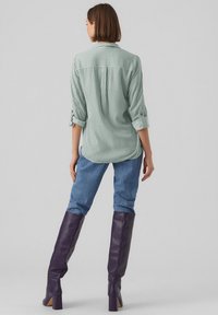Green and white striped long-sleeve shirt, paired with light blue jeans and knee-high purple leather boots. Buttoned sleeves rolled up slightly.