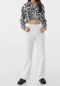 Camisa recortada en blanco y negro con patrones abstractos, combinada con pantalones de pierna ancha blancos de cintura alta y zapatos de plataforma negros.