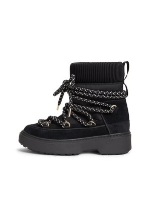Botte d'hiver noire avec une semelle épaisse, un revers en tricot, et des lacets ronds à motifs enroulés plusieurs fois autour de la cheville.