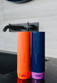 Zwei zylindrische Körpersprühflaschen, eine orange und eine dunkelblau, beide mit gerillter Textur und beschriftet mit "Warm-Up" und "Sport Recovery."