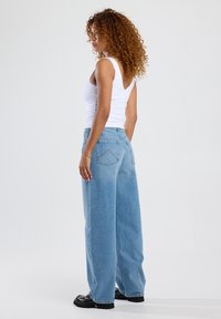 Lichteblauwe jeans met wijde broekspijpen van denim, voorzien van achterzakken en een relaxte pasvorm. Gecombineerd met een mouwloos wit topje.