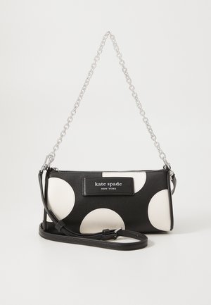 Black and white polka dot handbag featuring a smooth leather exterior, silver chain strap, and a branded plaque on the front.