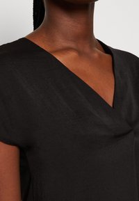 Top nero leggero con scollatura a V e maniche corte, caratterizzato da una texture morbida e un fit rilassato. Drappeggio notevole nella zona del busto.