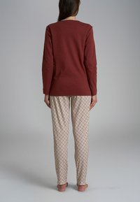 Maglietta a maniche lunghe bordeaux con scollatura rotonda abbinata a pantaloni da pigiama leggeri con motivo a rombi in beige e marrone.