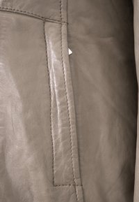 Gray leather material featuring smooth texture and subtle sheen, with a straight seam and a small tag protruding from the side.