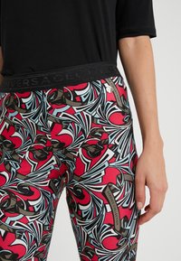 Tajtpassande leggings med ett djärvt röd, svart och blått virvlande mönster. Har en svart texturerad midjeband märkt "Versace Collection."