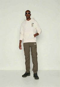 Balta džemperio su gobtuvu priekinio dizaino, derinama su alyvuogių žalių krovinių kelnėmis ir juodais žygių batais. Papildyta baltais akiniais nuo saulės.