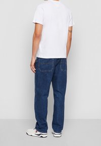 Vit bomull t-shirt med kort ärm, kombinerad med mörkblå denimjeans, som har en avslappnad passform och två bakfickor.