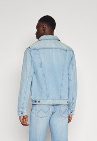 Jasnoniebieska kurtka dżinsowa z klasycznym kołnierzem, długimi rękawami i detalami przeszycia. Posiada zapięcia na guziki i luźny krój.