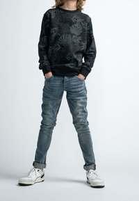 Černá mikina se šedým listovým vzorem, doplněná o vybledlé modré džíny a bílé tenisky s černými akcenty. Ležérní střih a styl.