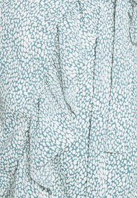 Jasnoniebieska bluzka z białym abstrakcyjnym wzorem, z falbaniastymi akcentami i miękką, gładką teksturą materiału.