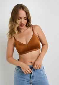 Reggiseno in satin marrone con forma triangolare, spalline regolabili e design senza cuciture. Indossato con jeans in denim blu a vita alta.