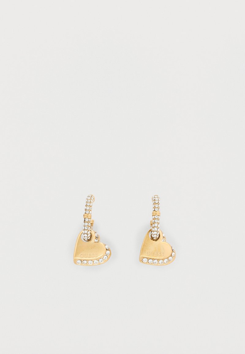 Gold-tone heart-shaped earrings featuring a smooth surface, rhinestone accents, and a textured hoop design with "GUESS" engraving.