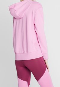 Sudadera rosa con capucha con cordón, fabricada en un material suave y con puños acanalados. Combinada con mallas color burdeos que tienen paneles en bloque de color rosa y burdeos.