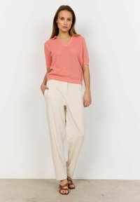 Coral knitted sweater with a V-neck and short sleeves, paired with light beige tapered trousers and brown cross-strap sandals.