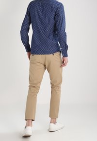 Navy button-up shirt with small white polka dots, paired with beige chinos and white sneakers, viewed from behind.