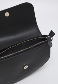 Black leather handbag with a smooth texture, featuring a gold snap closure and a zippered pocket inside. Minimalist design with clean lines.