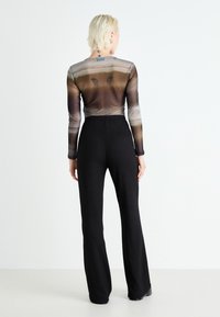 Top transparent à manches longues avec des rayures brunes dégradées, associé à un pantalon large noir à côtes taille haute. La vue de dos met en avant des imprimés de papillons.