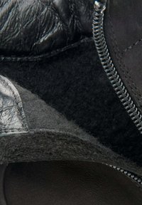 Czarne botki za kostkę z teksturowanej skóry, z wełnianym podszyciem i bocznym zamkiem błyskawicznym. Podeszwa jest gładka i ciemna, z zaokrąglonymi brzegami.