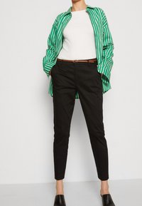 Grön och vit randig skjorta med knappar, vit topp under, svarta slim-fit byxor, brun bälte och svarta slip-on skor.