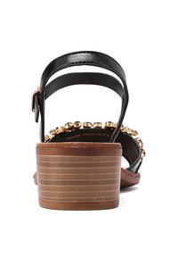 Sandali con tacco marroni e neri, caratterizzati da una punta arrotondata, cinturini neri e un accento decorativo di perle dorate attorno alla caviglia. Tacco marrone con texture.