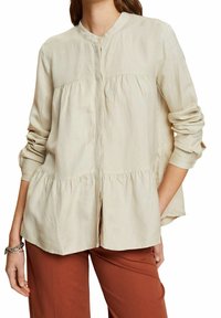 Blusa ligera beige con cuello mandarín, cierre frontal de botones y dobladillo fruncido. Mangas largas con puños enrollados.