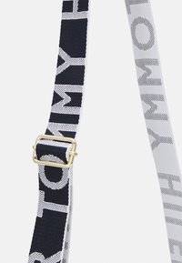 Sangle en tissu tressé noir et blanc avec boucle en métal doré réglable et un grand motif de texte en gras de chaque côté.