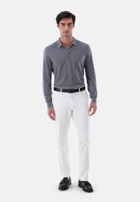 Graues Longsleeve-Polo mit Kragen und zwei Knöpfen, kombiniert mit weißen Hosen und schwarzen Loafers; glänzender Stoff und taillierte Passform.