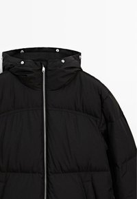 Schwarze Pufferjacke mit Reißverschlussfront, Kapuze und Druckknöpfen. Der Stoff ist glatt mit einer gesteppten Textur und gepolsterten Bereichen.