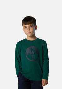Camiseta verde de manga larga hecha de tela suave, que presenta un gran logotipo circular negro con el texto "NORTH SAILS" y detalles.
