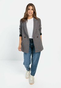Dubbelgeknoopt geruit blazer in grijs, blauw en roze tinten; heeft grote revers en opgerolde mouwen. Gepaard met high-waisted jeans en sneakers.