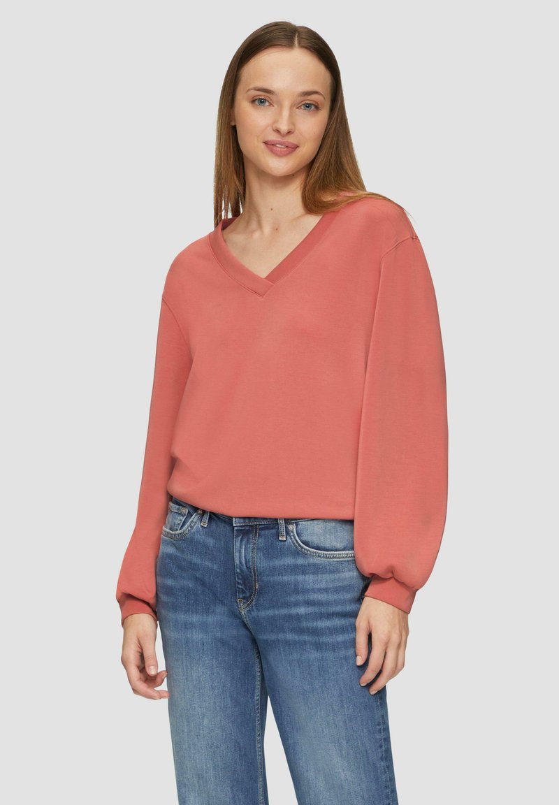 Koraal kleurige V-hals sweatshirt met ballonmouwen, van zachte stof en met een ontspannen pasvorm, gecombineerd met blauwe jeans.