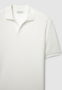 Polo blanc en tissu texturé, avec un col en V et des manches courtes. L'étiquette indique "CALLIOPE", taille L.