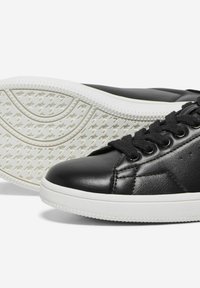 Baskets en cuir noir avec semelles en caoutchouc blanches, design à lacets, accents texturés et motif de bande de roulement circulaire sur la semelle extérieure.