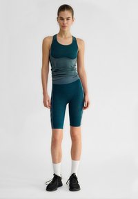 Teal atletisk tanktopp med texturerad panel och matchande cykelshorts. Har en figurnära design och kontrasterande sidodetaljer. Skor och strumpor ingår.