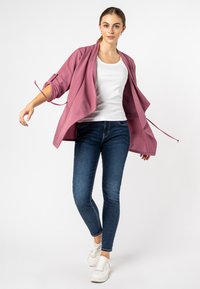 Hellrosa offene Jacke aus weichem Stoff, kombiniert mit einem weißen Tanktop, dunkelblauen Skinny-Jeans und weißen Sneakers.