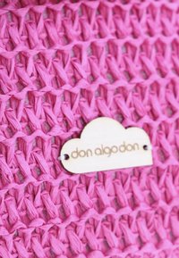 Tela tejida de color rosa con un acabado texturizado. Presenta una etiqueta de madera en forma de nube con "don algo don" grabado.