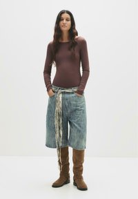 Maglia marrone a maniche lunghe e culotte in denim azzurro chiaro con una cintura a fantasia annodata. Stivali al ginocchio in suede marrone completano l'outfit.