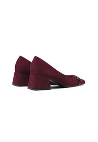 Scarpe in suede bordeaux con tacco a blocco e punta affusolata, dotate di un dettaglio decorativo in metallo nella parte anteriore. Texture liscia e design moderno.