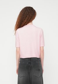 Ροζ ανοιχτόχρωμο πλεκτό πουλόβερ με κοντά μανίκια και στρογγυλή λαιμόκοψη, φορεμένο με ψη λόμεσα σκούρα γκρι τζιν με επένδυση στο πίσω μέρος.