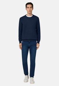 Sweat-shirt bleu marine avec encolure ronde, poignets et taille côtelés, assorti à un jean bleu foncé et des baskets blanches.