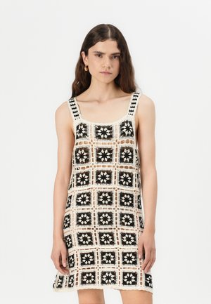 Häkelkleid mit Quadratmotiv in Schwarz und Creme, mit Rundhalsausschnitt und dünnen Trägern; offenes Gewebe-Design lässt die Haut darunter durchscheinen.