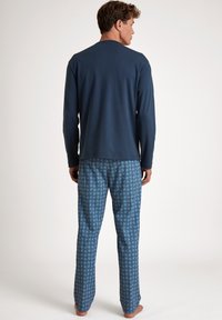 Langarm navy top gecombineerd met gestreepte blauwe pyjamabroek. De broek heeft een geometrisch ontwerp in donkerblauw op een lichtere blauwe achtergrond.