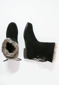 Botas de tobillo de ante negro con forro de piel sintética, que cuentan con botones laterales y lazadas en la parte posterior. La suela es plana con un ligero tacón.