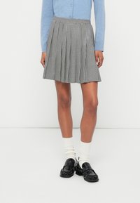 Plisowana spódnica w czarno-białą kratę z elastycznym paskiem w talii. Zestawiona z jasnoniebieskim kardiganem, białymi skarpetkami i czarnymi mokasynami.