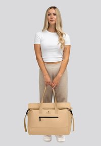 Borsa a tracolla beige con due manici, tasca con zip nera e logo. Realizzata in materiale resistente con una texture liscia.